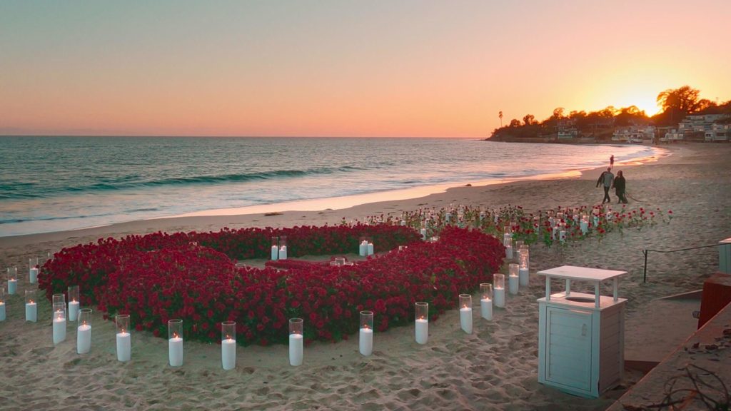 Kourtney Kardashian and Travis Barker walk along the beach towards a sea of roses as Travis prepares to propose