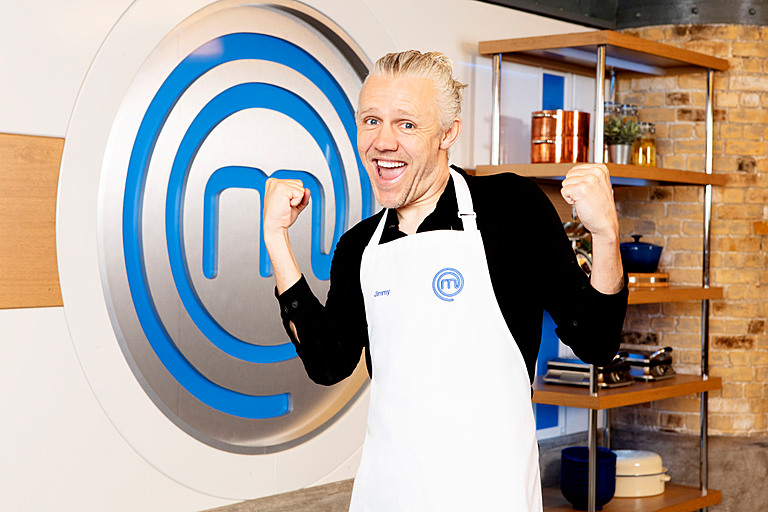 Jimmy Bullard holds hands in fists in front of MasterChef sign to left.