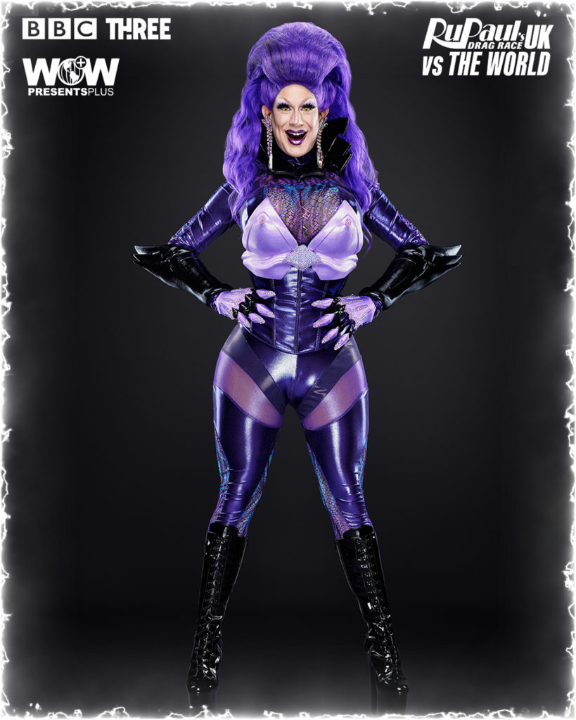 Jimbo stands with her arms on her waist in a purple ensemble for a promo for RuPaul Drag Race UK VS The World Season 1
