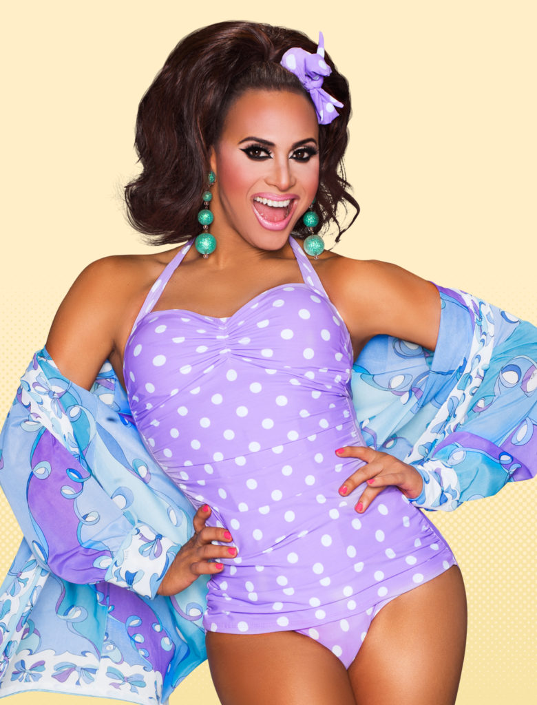 Drag Queen Naysha Lopez wears a purple and white polka dot top bodice with a glittery sheer shawl over her shoulders in a 1950s esque look for a Promo for RuPaul Drag Race Season 8