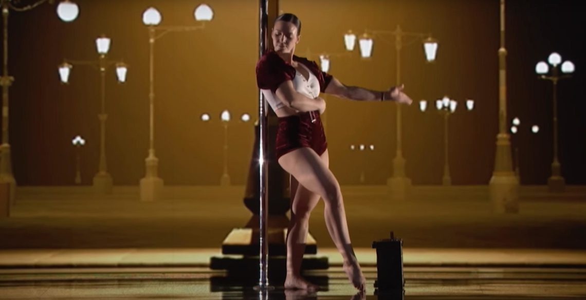 Kristy Sellars holds left arm out while pole dancing.