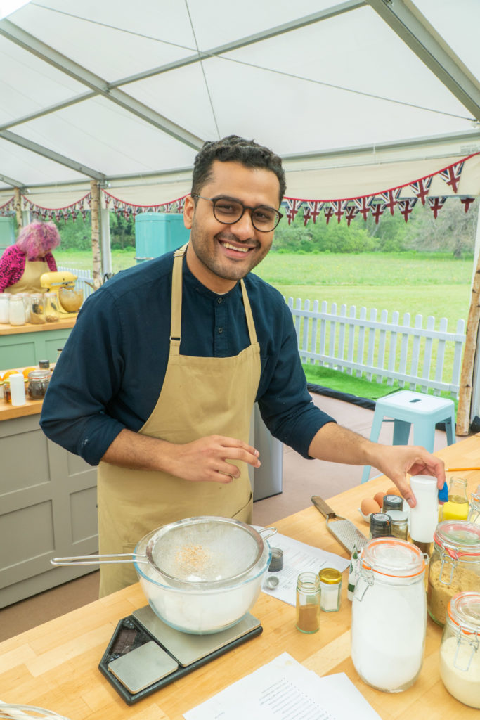 Abdul baking in the tent wearing blue jumper and beige apron