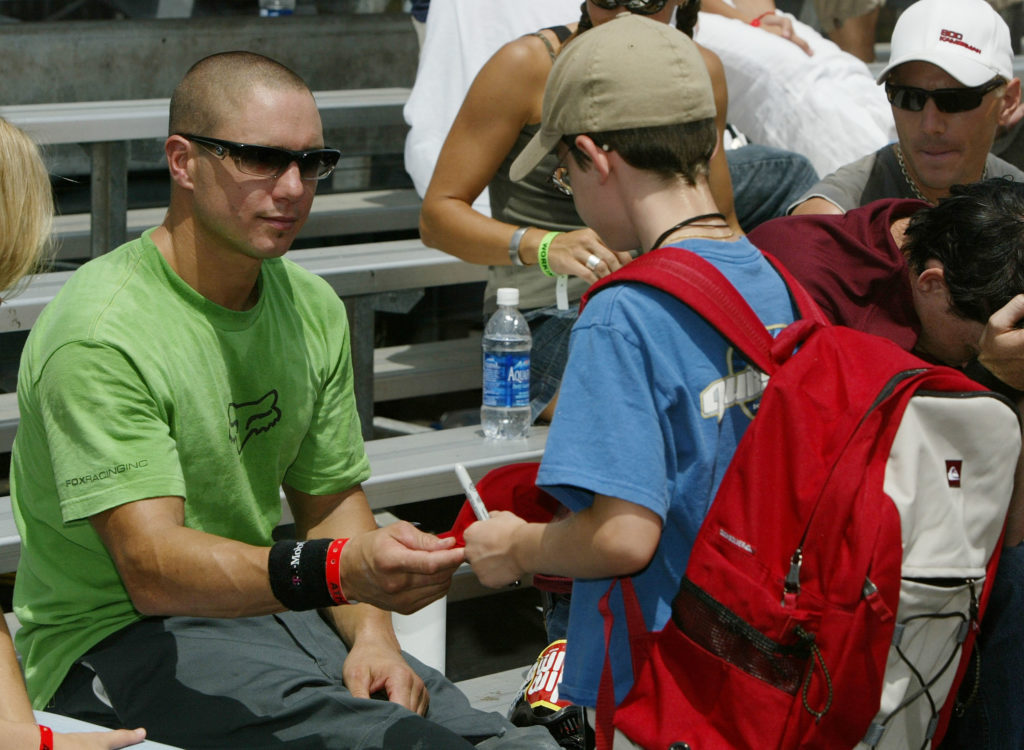 Dave Mirra gestures to sign his autograph for a child, he wears black sunglasses and a green t-shirt