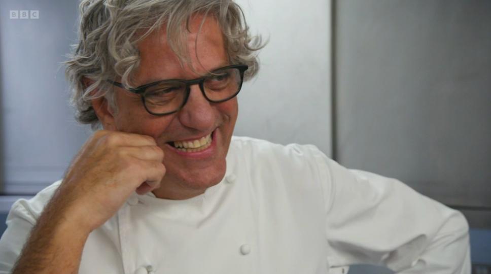 Giorgio Locatelli dressed in chef's whites laughs resting his face on fist