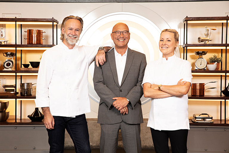 Marcus Wareing, Gregg Wallace, Anna Haugh opse smiling for the camera in a promo shot for MasterChef The Professionals 2022, Marcus and Anna wear chef whites and Gregg wears a grey suit