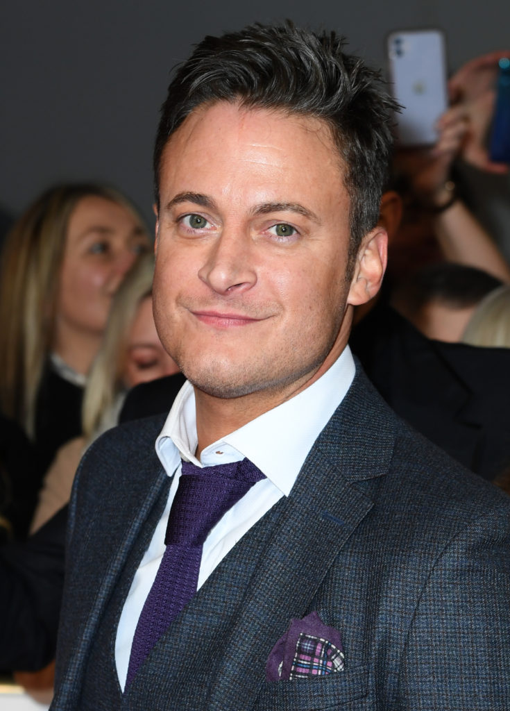 Gary Lucy wears white shirt and navy suit jacket and dark purple tie at the National Television Awards 2020
