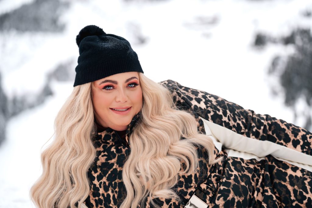 Gemma Collins smiles wearing leopard print snow suit and black bobble hat posing in the snow