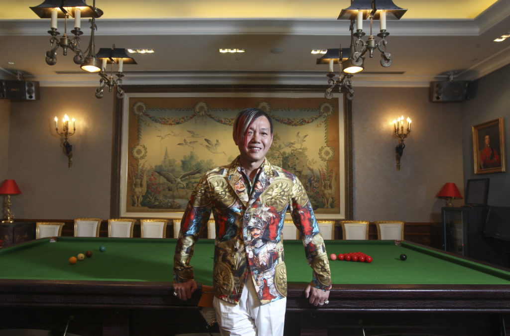 Stephen Hung poses in front of pool table wearing colourful suit jacket and white trousers