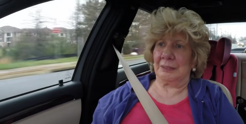 Nanny Faye sits in passenger seat of car wearing pink top and purple jacket