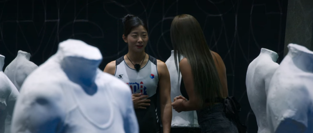 Jang Eun-Sil speaks to another contestant standing among torso statues on Physical 100