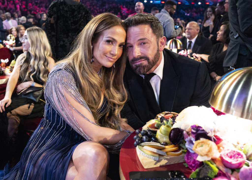 (L-R) Jennifer Lopez in black sparkly dress next to Ben Affleck in black tie suit sat at table at the Grammy awards