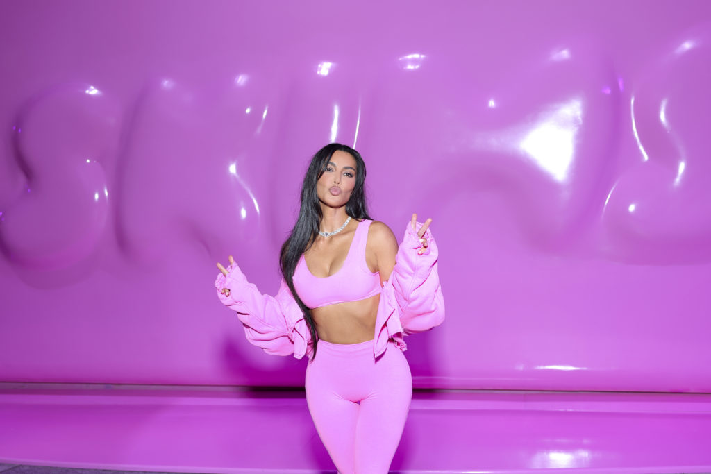 Kim Kardashian holds peace sign up with both hands wearing pink outfit at SKIMS Valentine's Shop Pop-Up