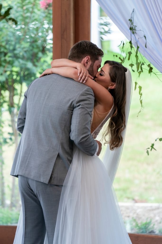 Matt Bolton wears grey suit with hands on Colleen Reed's back in white dress and veil on head, with wrapped arms around him.