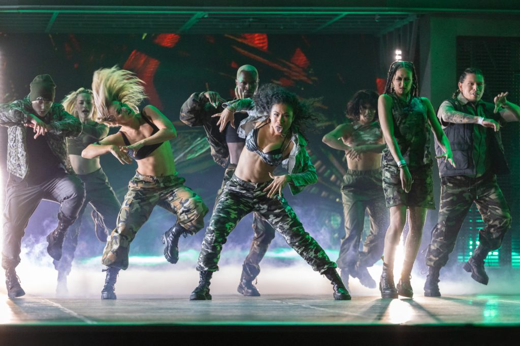 Celine's dance troop in Dance 100 dressed in army camouflage whip their hair back and forth on stage