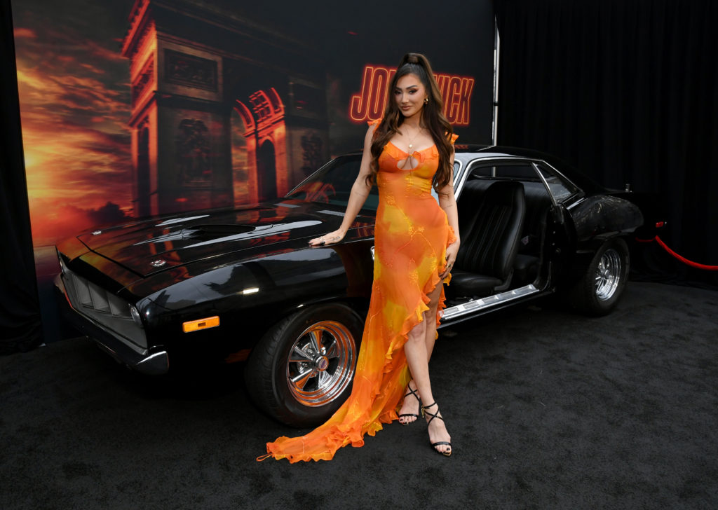Francesca Farago in orange dress leaning on black car at John Wick 4 premier
