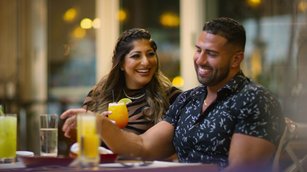 Arti and Jamal smile together having drinks at table filming Indian Matchmaking