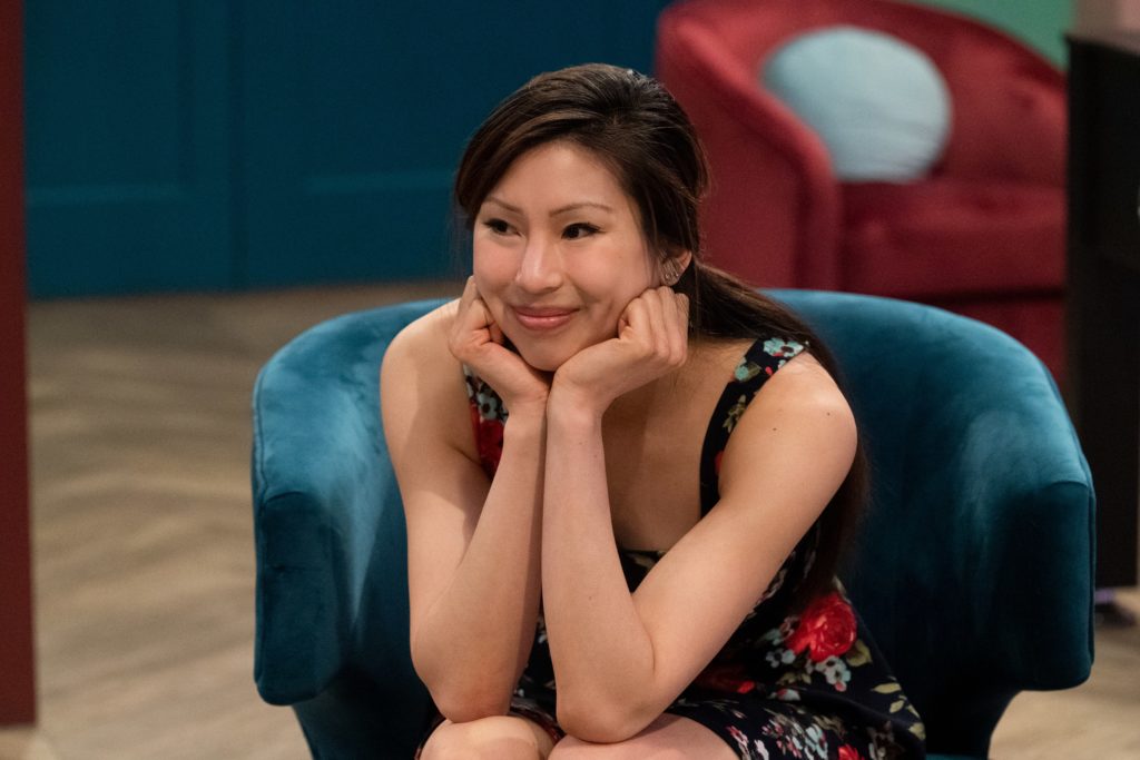 Wendy Kong sits in blue chair smiling in dress, with her hands under her chin.