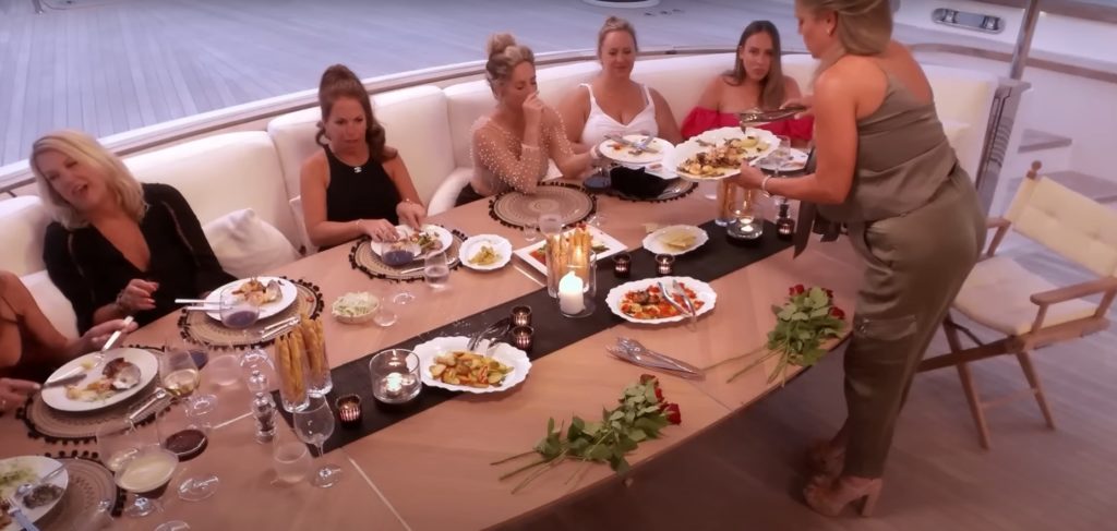 Below Deck Sailing Yacht season 4 guests having a meal at a large table while one guests is stood up to serve her friends 