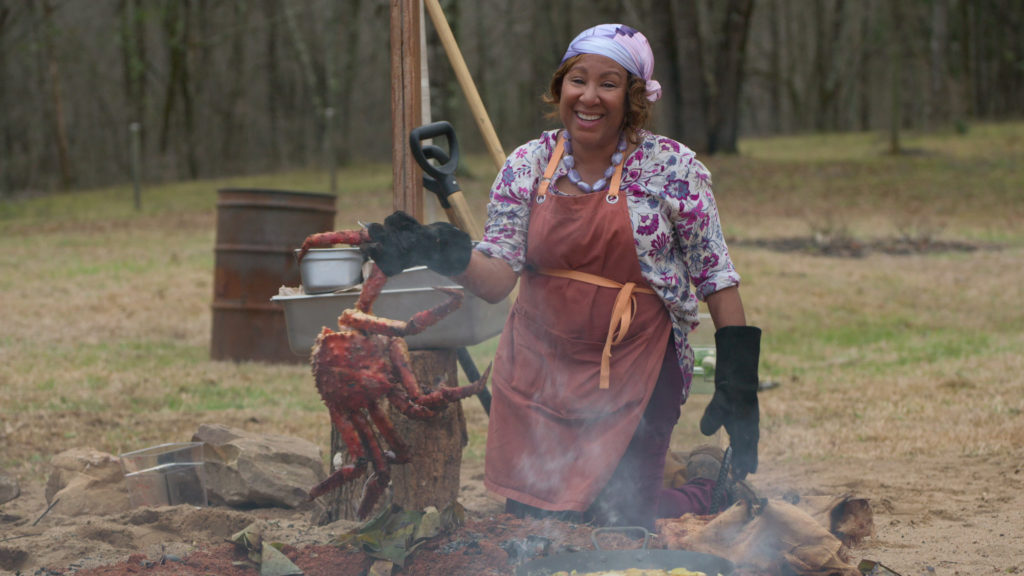 Delilah Winder wears apron holding crab on Barbecue Showdown