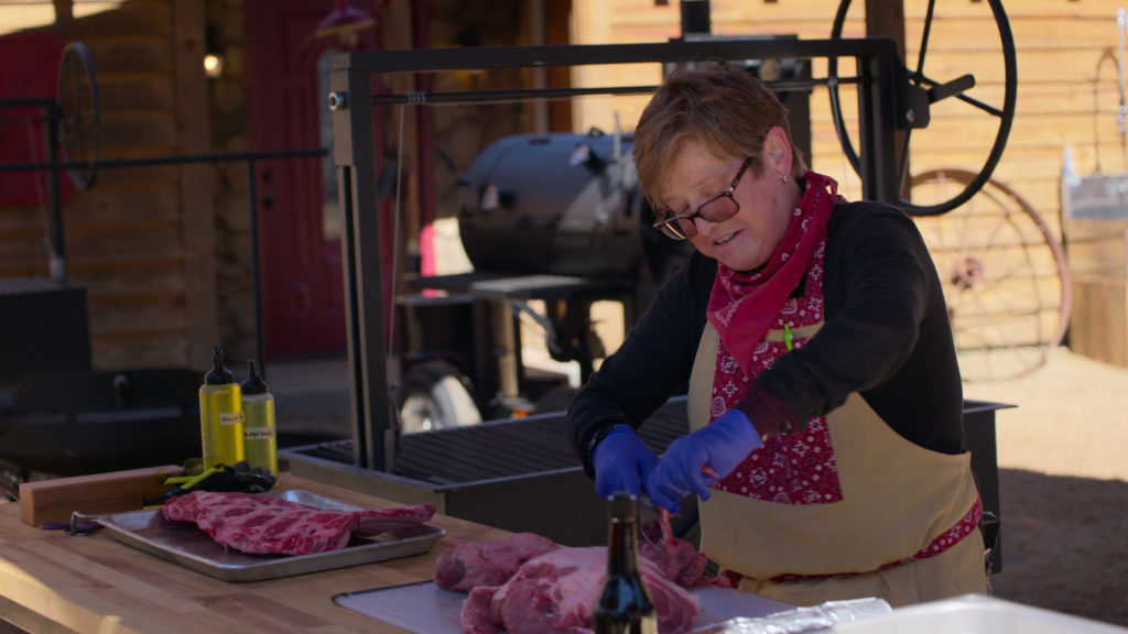 Cindy Hayter prepares meat wearing gloves and an apron looking down at food on Barbecue Showdown