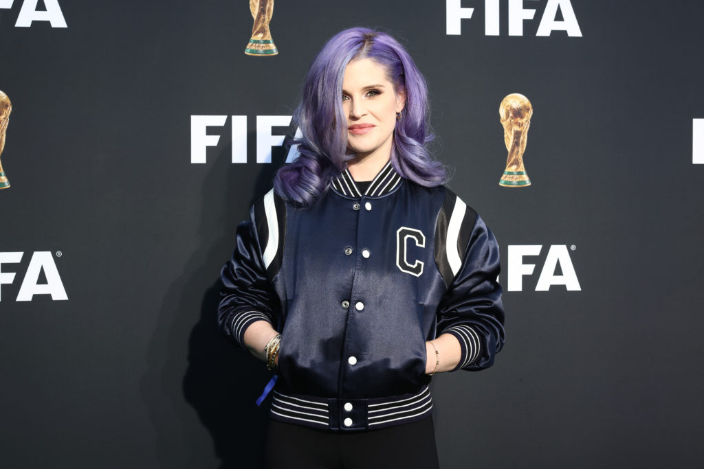 Kelly Osbourne stands smiling for camera with hands in pockets wearing black jacket at IFA FWC26 Emblem Launch