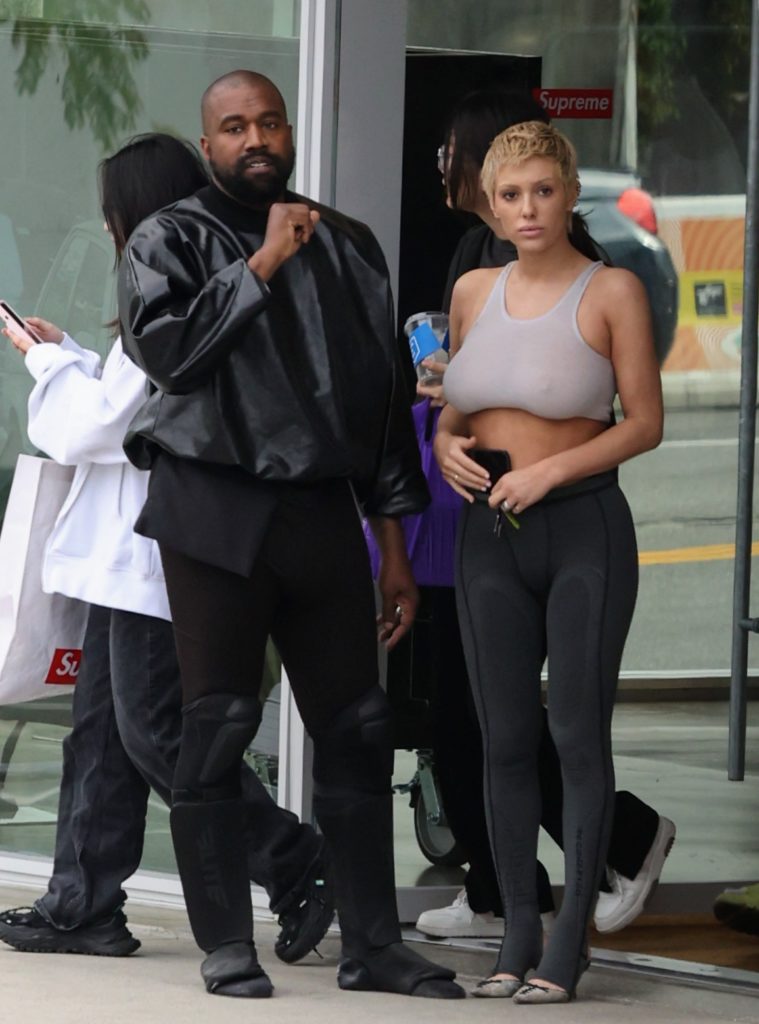 Kanye West and Bianca Censori stand together looking at camera walking down LA sidewalk