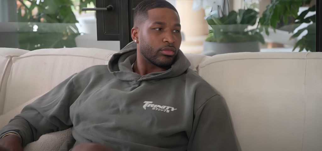 Tristan Thompson looks across at someone out of shot sitting on sofa wearing grey hoodie