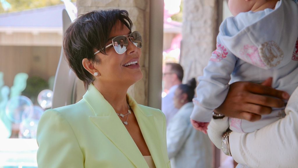 Kris Jenner wears lemon color blazer and sunglasses looking up at Tatum Thompson who is out of shot